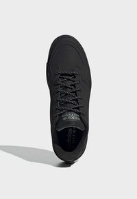 Scarpa atletica nera con tomaia testurizzata, dotata di lacci neri e logo sulla linguetta. Design minimalista con punta arrotondata.