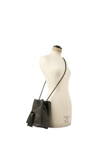 Sac seau en cuir noir avec détail pompon exposé sur un mannequin beige sur fond blanc.