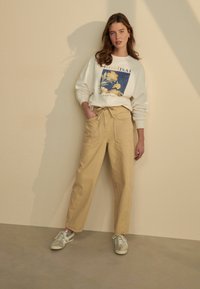 Pantalons large à rayures beige clair avec deux poches avant, associés à un sweat-shirt blanc affichant un design graphique floral bleu.