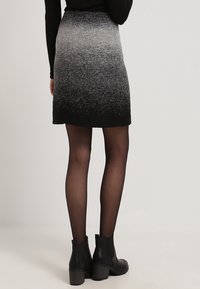 Svart och grå ombre kjol, knälång, tillverkad av strukturerat tyg. Har en solid svart fåll och är kombinerad med svarta ankelskor.