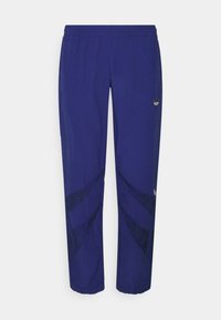 Pantaloni jogger viola realizzati in un tessuto leggero, con un motivo astratto nero sui lati, vita elastica e un piccolo logo decorativo.