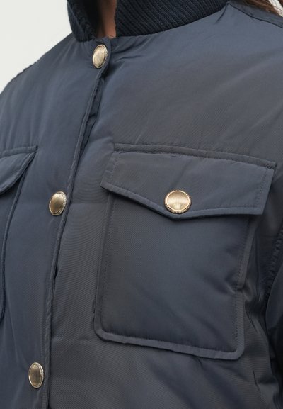 Tumedat sinine paksu voodriga jakk, millel on ribikrae, kuldsed nööbid ja kaks esiset kotti kuldsete detailidega. Sile tekstuur.