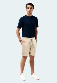 Navy blue short-sleeve t-shirt paired with beige shorts featuring a drawstring, rolled hems, and white sneakers. Plain background.