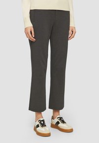 Pantalons gris légers avec une coupe droite, dotés de coutures décoratives et de poches avant, associés à des baskets blanches et brunes.