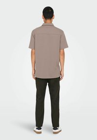 Kortärmad, beige polo-shirtd med en bakre söm, kombinerad med mörkgröna byxor och vita sneakers med svarta detaljer.
