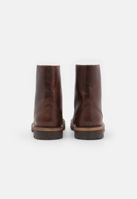 Hnědé kožené kotníkové boty s hladkým povrchem, šitými bočními panely a dřevěnou podešví. Design se vyznačuje zaoblenou špicí a minimálním použitím kovových prvků.