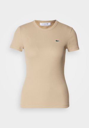 T-shirt en coton côtelé beige à manches courtes, col rond, forme ajustée, avec un petit logo vert Lacoste sur la poitrine gauche.