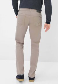 Pantaloni marroni chiari con taglio dritto, dotati di due tasche posteriori, dettagli di cucitura sottile e abbinati a scarpe blu.