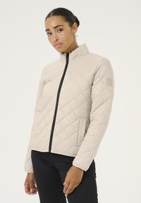Veste matelassée beige clair avec un col montant, fermeture éclair noire et poches latérales. Présente un motif en losanges et un logo sur la manche gauche.