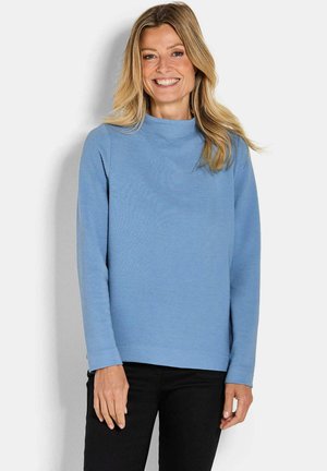 Haut à manches longues bleu côtelé avec un col montant, présentant une coupe décontractée. Porté avec un pantalon noir, le matériau semble doux et texturé.