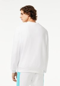 Sudadera blanca de manga larga, con cuello redondo, textura suave y puños acanalados, combinada con pantalones deportivos de color azul claro.