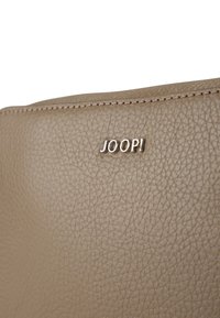 Torebka wykonana z brązowej skóry, z fakturowanym wykończeniem i subtelnym połyskiem, z logo "JOOP!" wytłoczonym z przodu.