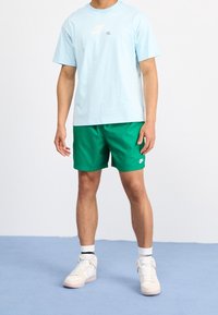 Světle modré bavlněné tričko s bílým logem Nike, spárované se zelenými šortkami a bílými teniskami s růžovými akcenty a černými pruhy.