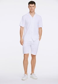 Witte kortemouwen overhemd met knopen, gecombineerd met bijpassende shorts. Beide gemaakt van lichte stof, met een gladde textuur en minimalistisch design.