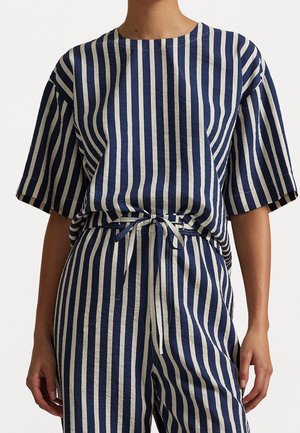 Personne portant un haut à manches courtes rayé verticalement bleu marine et blanc et un pantalon assorti à cordon de serrage, la taille nouée avec un nœud.