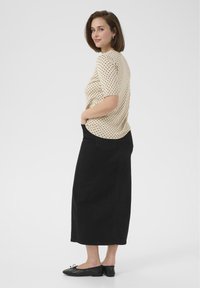 Haut beige à pois, manches courtes, associé à une jupe midi noire en tissu texturé, avec des ballerines noires ornées d'un nœud.