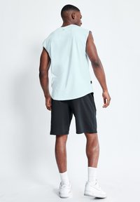 Top sin mangas de color azul claro con dobladillo redondeado, combinado con pantalones cortos negros. La modelo lleva zapatillas blancas y calcetines blancos a la altura del tobillo.