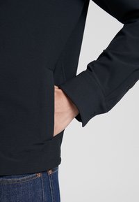 Sort jakke lavet af glat stof, med en sidelomme og knapmanchetter. Designet er tætsiddende med et minimalistisk æstetik.