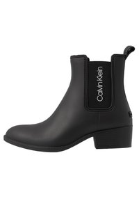 Bottine noire en caoutchouc lisse avec panneaux élastiques sur les côtés, talon bloc, et logo "Calvin Klein" sur le côté. Design à bout arrondi.