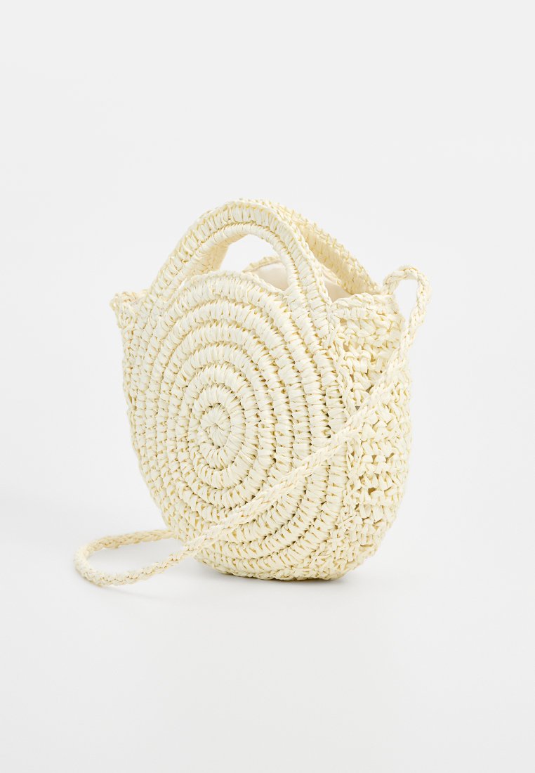Bolsa redonda tejida, hecha de fibras naturales beige. Presenta dos asas cortas y una correa para el hombro larga y delgada. Superficie texturizada con un patrón en espiral.