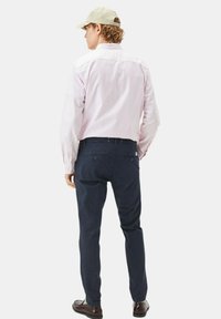 Camicia a righe rosa chiaro con bottoni, pantaloni blu navy e un cappellino beige chiaro. I pantaloni hanno tasche posteriori, la camicia ha un colletto classico e maniche lunghe.