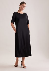 Czarna sukienka midi z krótkimi rękawami, okrągłym dekoltem, bocznymi kieszeniami oraz gładką, elegancką fakturą. Noszona z czarnymi sandałami na wysokim obcasie z paskami.