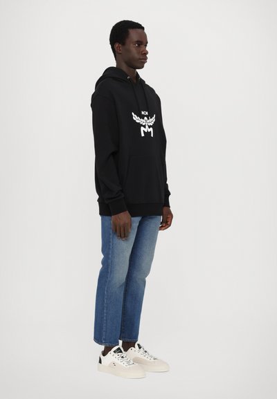 Hoodie noir avec logo blanc au centre, associé à un jean bleu clair et des baskets blanches. Tissu doux avec une coupe décontractée.