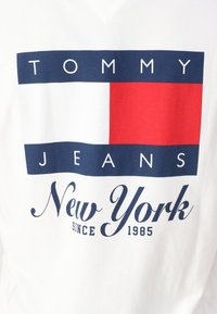 Hvit bomulls T-skjorte med marineblå og rød rektangulær logo med teksten "TOMMY JEANS" og "New York siden 1985". V-hals design.