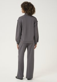 Siv set loungewear, ki vsebuje sproščen pulover s visokim ovratnikom in spuščnimi ramenimi šivi, ter široke hlače, vse v mehkem materialu.