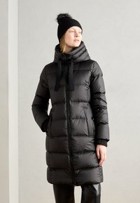 Giacca a vento nera con design a righe orizzontali, colletto alto e cappuccio regolabile. Abbinata a un berretto di maglia nero con pompon.
