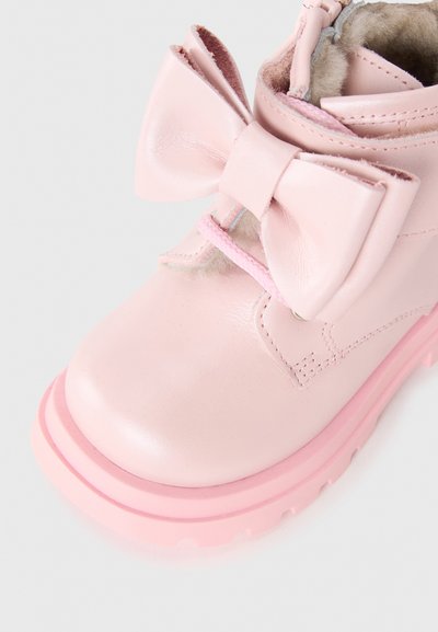 Botte de cheville en cuir rose avec un grand nœud à l'avant, dotée d'une finition texturée et d'une semelle en caoutchouc rose avec une traction subtile.