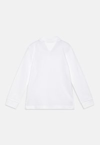 Polo shirt à manches longues blanche, avec un col classique, un empiècement en V à l'arrière et des poignets côtelés. Matière en coton douce et lisse.