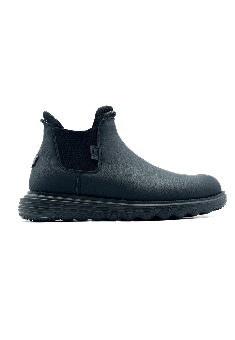 Botas de tobillo de cuero negro con paneles de malla elástica, punta redondeada y suela de goma texturizada que presenta un patrón ondulado para mayor agarre.