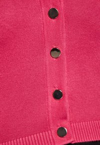 Rosa gestrickte Strickjacke mit gerippter Textur, fünf schwarzen Knöpfen auf der Vorderseite und einem taillierten Saum.
