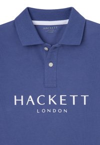 Polo majica u tamnoplavoj boji, izrađena od teksturirane tkanine. Ima klasičan ovratnik, dva dugmeta i bijeli logo "HACKETT LONDON" sprijeda.