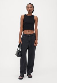Zwarte cropped tanktop, geknoopte zwarte wijde jeans en chunky platform schoenen. Accessoires omvatten een kleine zwarte handtas met banden.