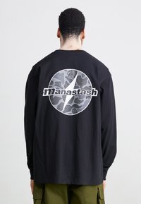 Schwarzes Langarm-T-Shirt mit einem kreisförmigen grauen Grafikdesign, das topografische Muster zeigt und das Wort "manastash" deutlich hervorhebt.