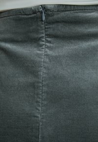 Falda de tejido verde oscuro con una textura suave, detalles de costura vertical y cierre de cremallera discreto en la parte posterior.