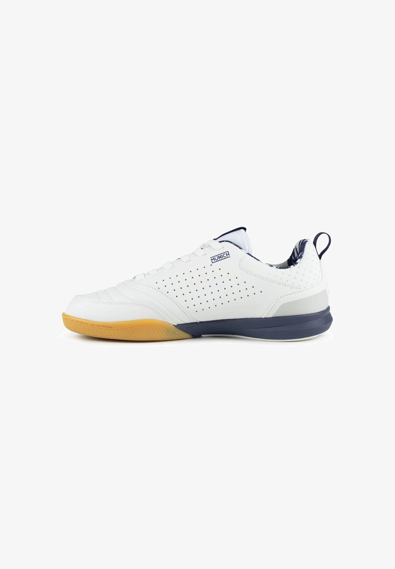 Chaussure de sport basse blanche avec côtés perforés, bordure bleu marine, semelle en gomme à l'avant et languette au talon. Marque Munich sur le côté.