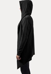 Cárdigan negro con capucha y un dobladillo asimétrico, textura suave, mangas largas y bolsillos frontales. Presenta un ajuste relajado y un diseño minimalista.