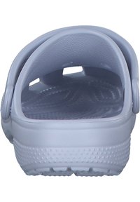 Zueco azul claro con parte trasera cerrada, plantilla texturizada, orificios de ventilación y protuberancias elevadas en la suela para proporcionar tracción. Material suave y flexible.
