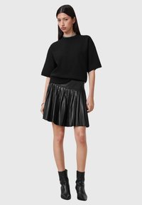 Maglione nero oversize a maniche corte abbinato a una mini gonna plissettata in pelle nera. La modella indossa stivaletti neri e una collana in argento.