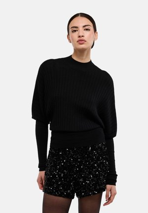 Haut noir en maille côtelée avec un col montant, associé à un short noir orné de sequins. La tenue comprend des manches longues et une taille cintrée.