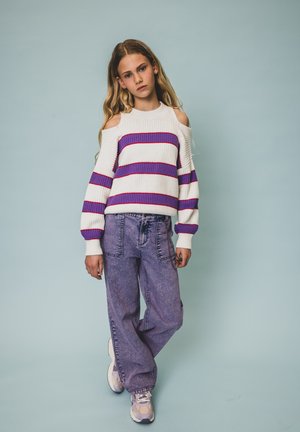 Witte gebreide trui met paarse en rode strepen, met een cold shoulder ontwerp. Gecombineerd met high-waisted, lichtpaarse denim broek en sneakers.