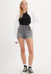Gray denim shorts with frayed hem, paired with a black ribbed tank top and an open white button-up shirt. Black high-top sneakers worn with white socks.