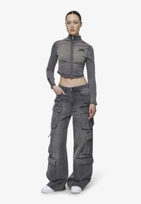 Gray cropped jacket with high collar, zip closure, and logo. Paired with wide-leg cargo pants featuring multiple pockets and zippers. White sneakers.