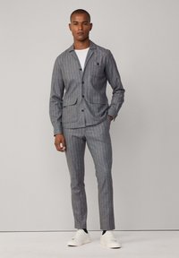 Completo grigio a righe sottili realizzato in tessuto texturizzato, completo di giacca con bottoni e due tasche, pantaloni su misura e sneakers bianche.