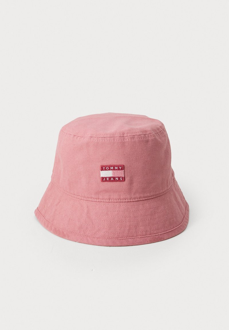 Chapéu de balde rosa feito de um tecido macio, com um rótulo da Tommy Jeans cosido na lateral e uma aba larga que se inclina para baixo.