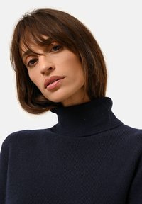 Pull à col roulé côtelé marine avec une silhouette ajustée et un tissu texturé, présentant un col haut et des détails de design minimaux.