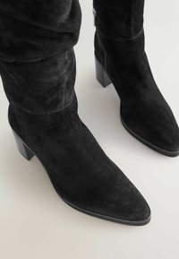 Zwarte suède enkellaarsjes met een spitse neus en een chunky hoge hak. Verkoper een zijrits en een zachte textuur, ontworpen voor comfort en stijl.